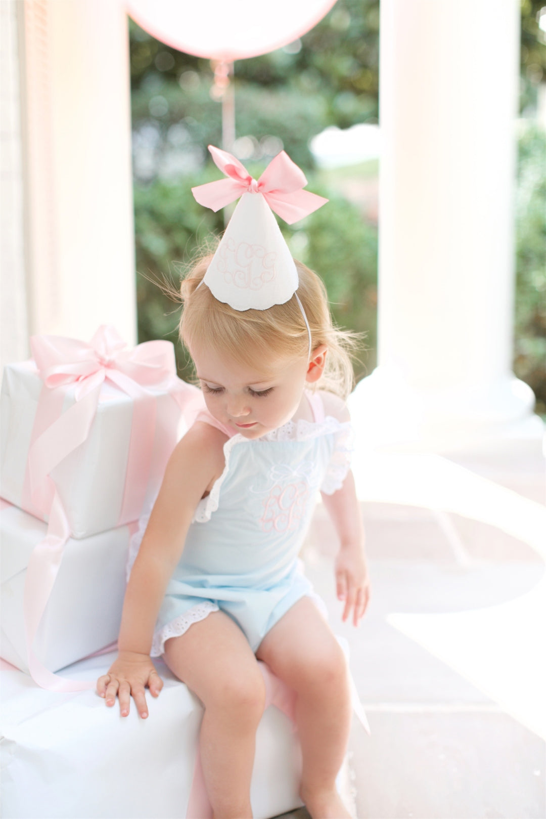 Little girl in a handmade party hat on white front steps beneath a pink bow banner