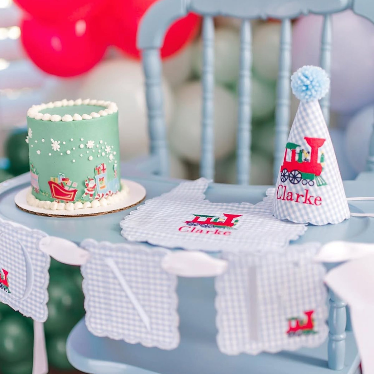 Toddler in a handmade party hat sitting outside a pink gingham play tent with a teddy bear